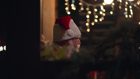Der-Weihnachtsmann-Trägt-Im-Winter-Ein-Geschenk-In-Seinen-Händen-Auf-Der-Straße,-Kommt-Zur-Tür-Und-Betritt-Das-Haus-Mit-Girlanden-Und-Weihnachtsdekorationen